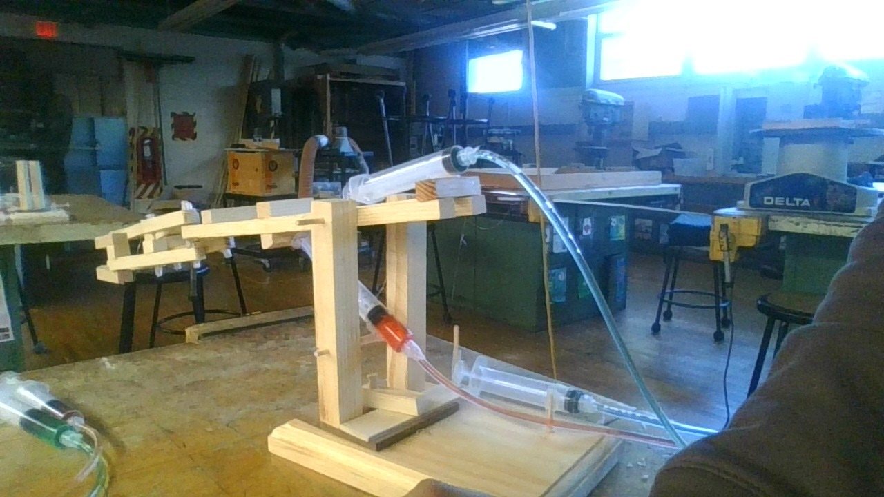 The complete wooden hydraulic arm on its base, with syringes and tubing